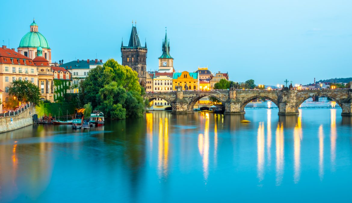 Illuminated Charles Bridge reflected in Vltava River. Evening panorama of Prague, Czech Republic. Panoramic shot